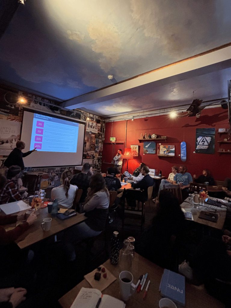 Indoor meeting with presentation slides displayed, attendees seated at tables.