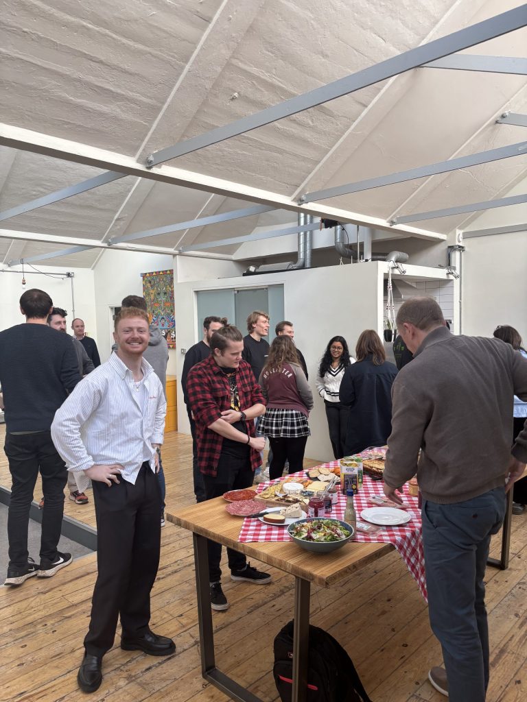 A group of people standing in a room. Some are smiling directly at the camera.