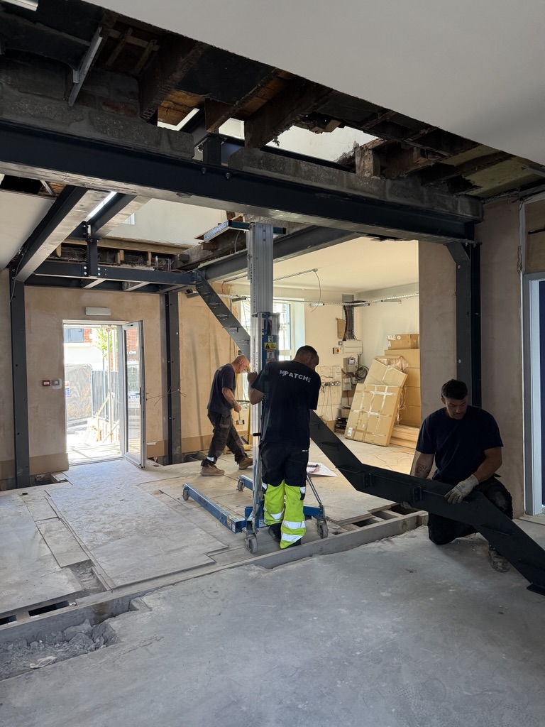 Three construction workers fitting dark metal staircase connecting ground and first floors at Courage House, Fanatic's new office.