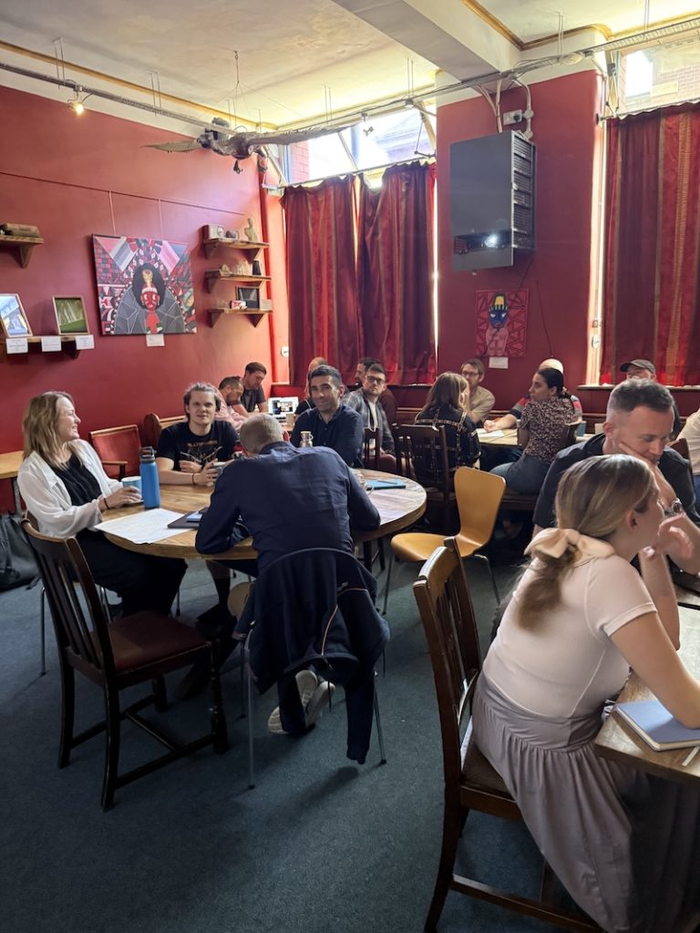 Fanatic employees seated at round wooden tables in the red-walled studio space with artwork displayed, engaged in small group discussions during a Vision Day planning session.