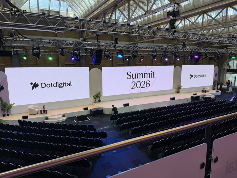 Wide-angle view of a conference auditorium set up for Dotdigital Summit 2026, with a large stage, projection screens, lighting rig, and chairs in rows