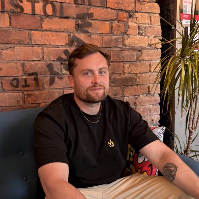Ben sat on a blue sofa in front of a brick wall