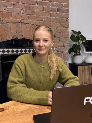 Emily in a green cardigan sitting behind a laptop