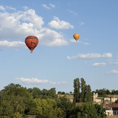 Two hot air balloons floating over the countryside near Amboise, France, above trees and rooftops.