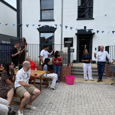 Ian speaks to guests gathered in a courtyard outside an office building decorated with blue and white bunting.